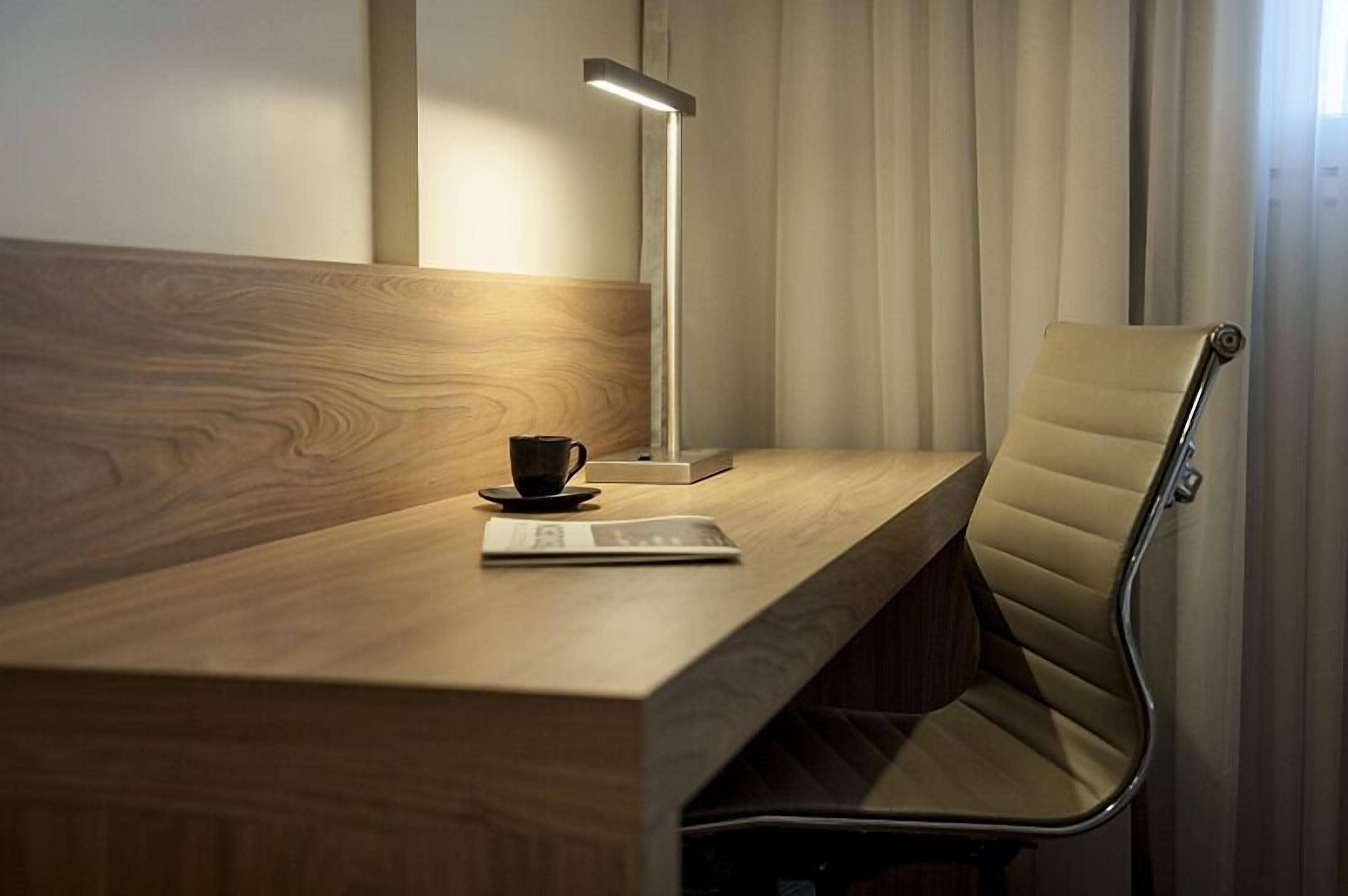A wooden desk with a modern lamp, a cup, and a menu.