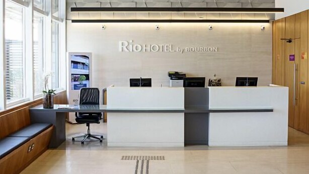 A hotel reception desk with a modern design, a textured ceiling, and a seating area with a bench. - Rio Hotel by Bourbon Campinas (Campinas)