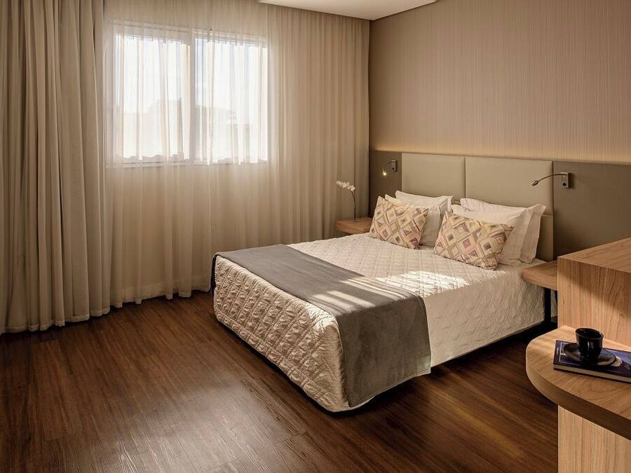 A hotel room with a bed, a bedside table, a window with curtains, and a wall-mounted TV.