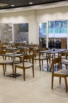 Un amplio comedor interior con varias mesas y sillas, grandes ventanales con vistas a árboles y una pared de piedra.