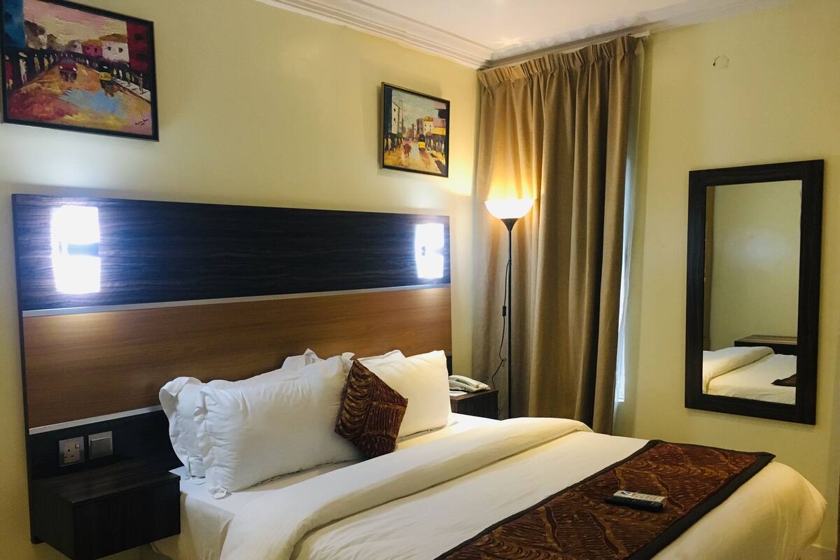 A hotel room with a large bed, a nightstand, a lamp, and a mirror.