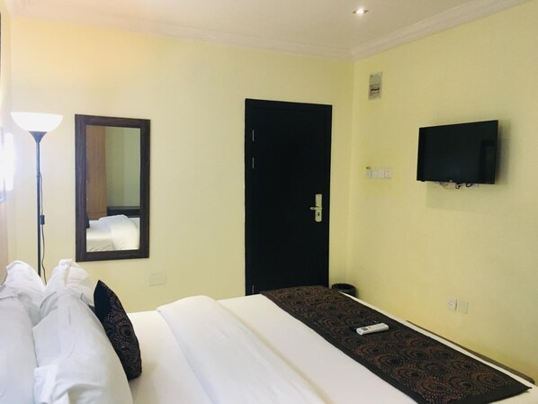 A hotel room with a bed, a black door, a television mounted on the wall, and a mirror.