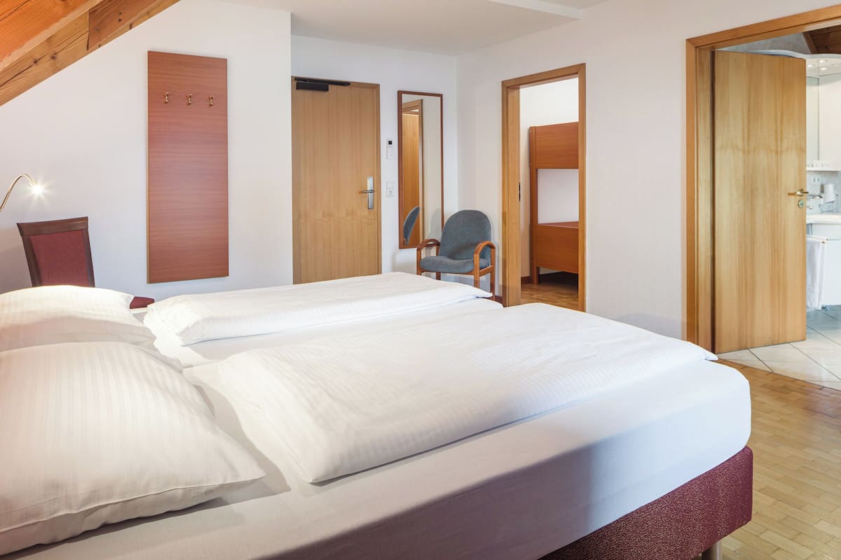 A bedroom with a large bed, a chair, and a wooden wardrobe.