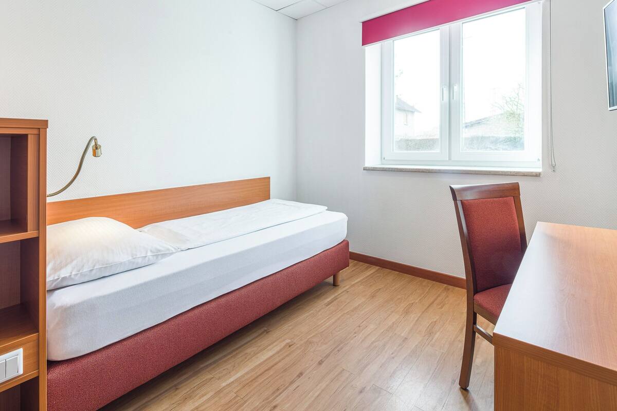 A room with a single bed, a wooden desk, and a chair.