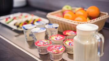 Una mesa de buffet con vasos de yogur, una cesta de fruta y una jarra de leche.