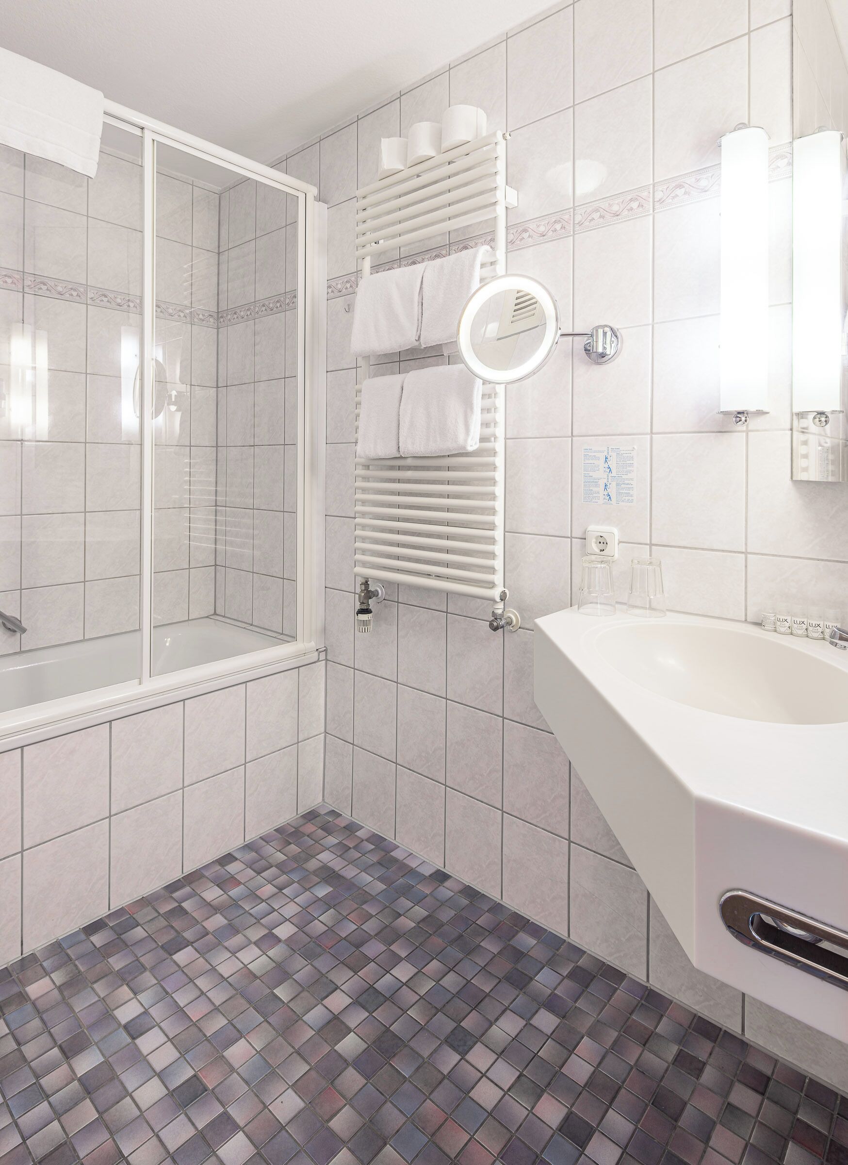 A modern bathroom with a glass shower enclosure, a white sink, and a tiled floor.
