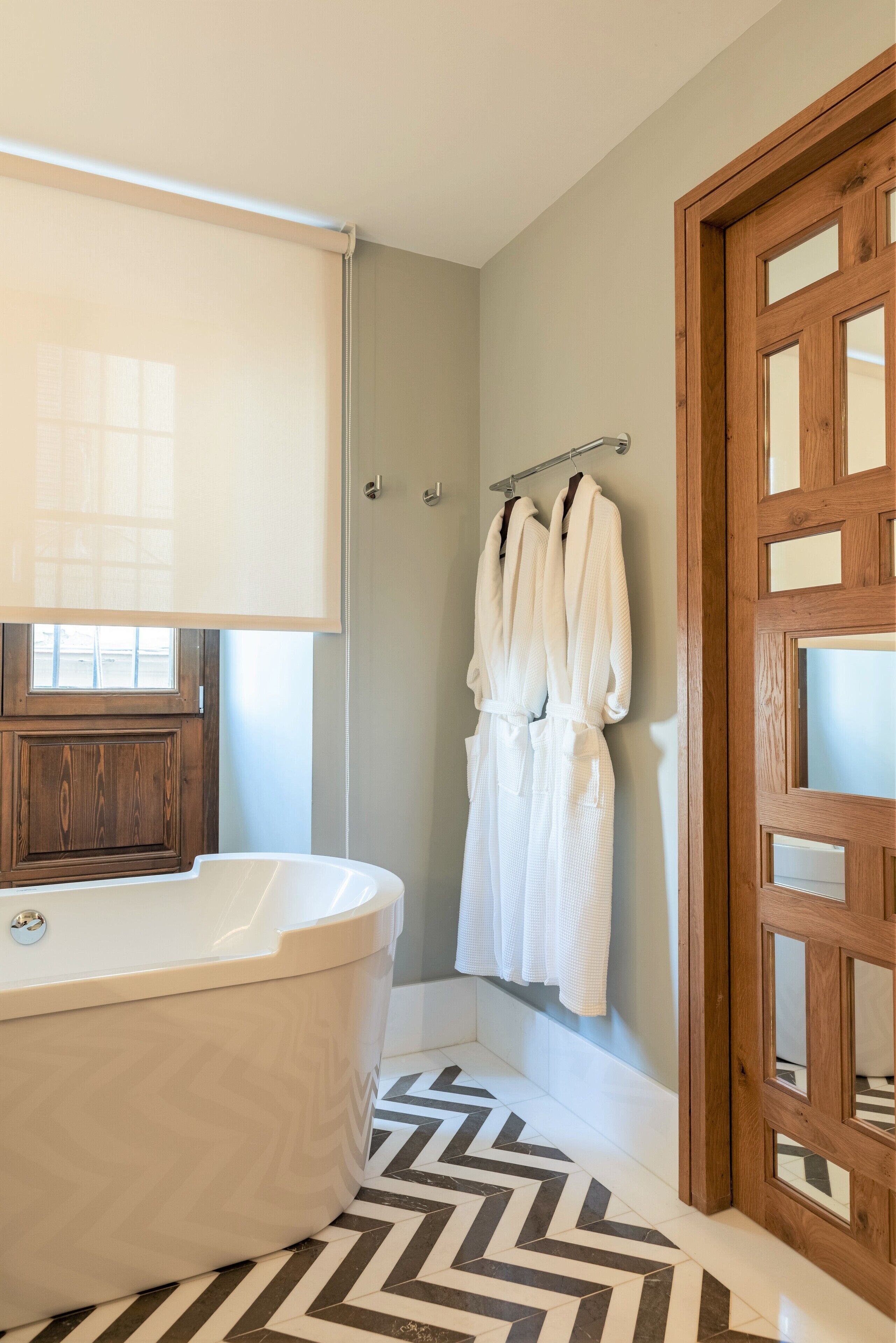 Ein modernes Badezimmer mit freistehender Badewanne, einer Holztür und einem gemusterten Boden.