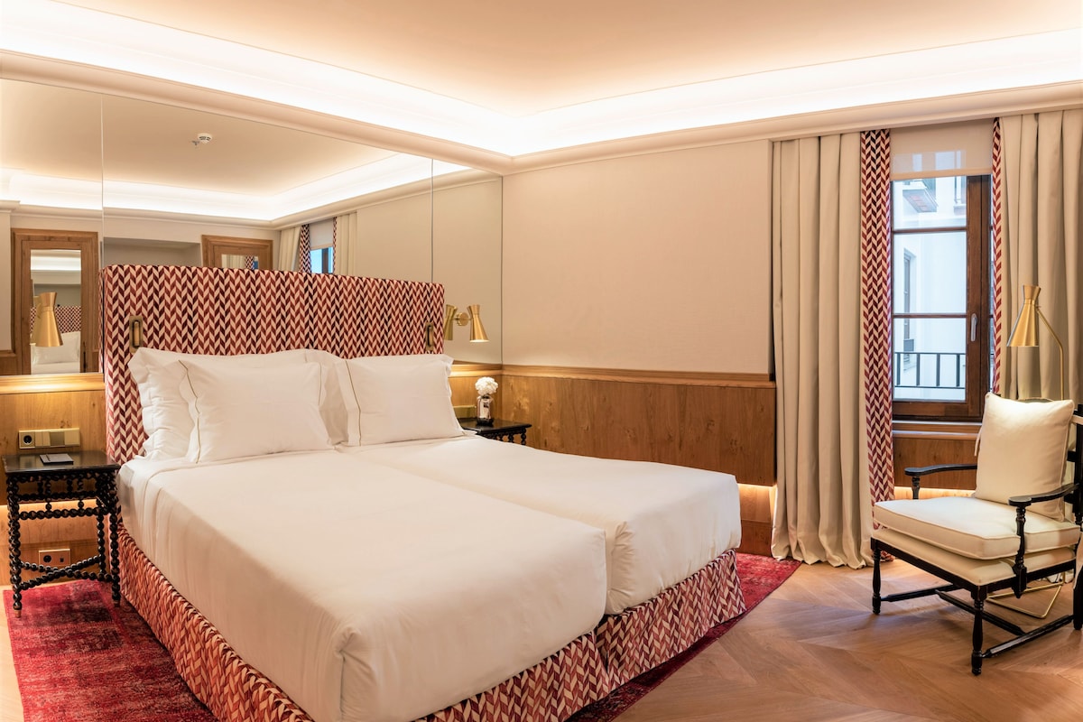 A hotel room with a large bed, a chair, a nightstand, a lamp, and a window with curtains.