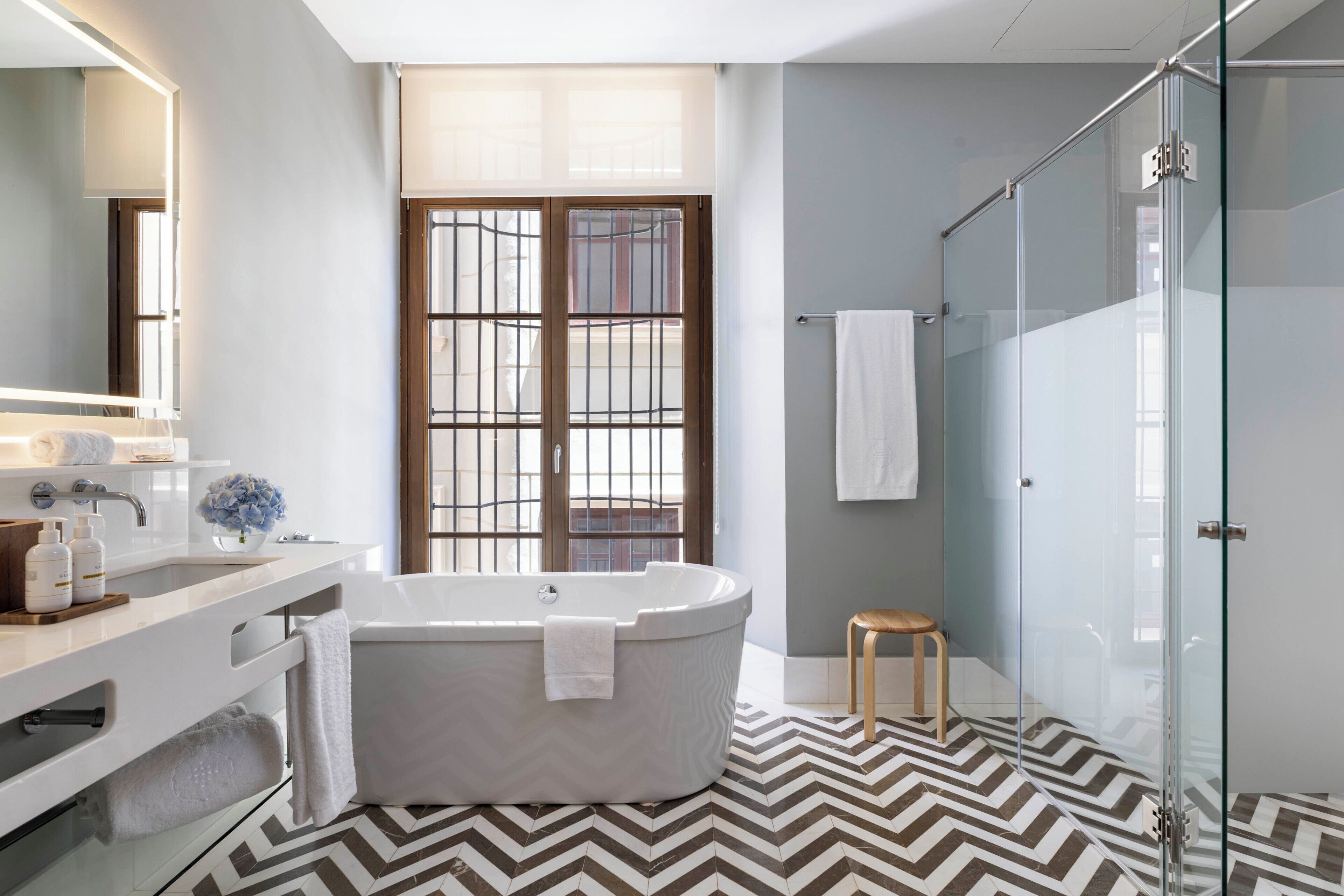 Un baño moderno con una bañera independiente, cabina de ducha con mampara de cristal y un amplio ventanal con vistas.