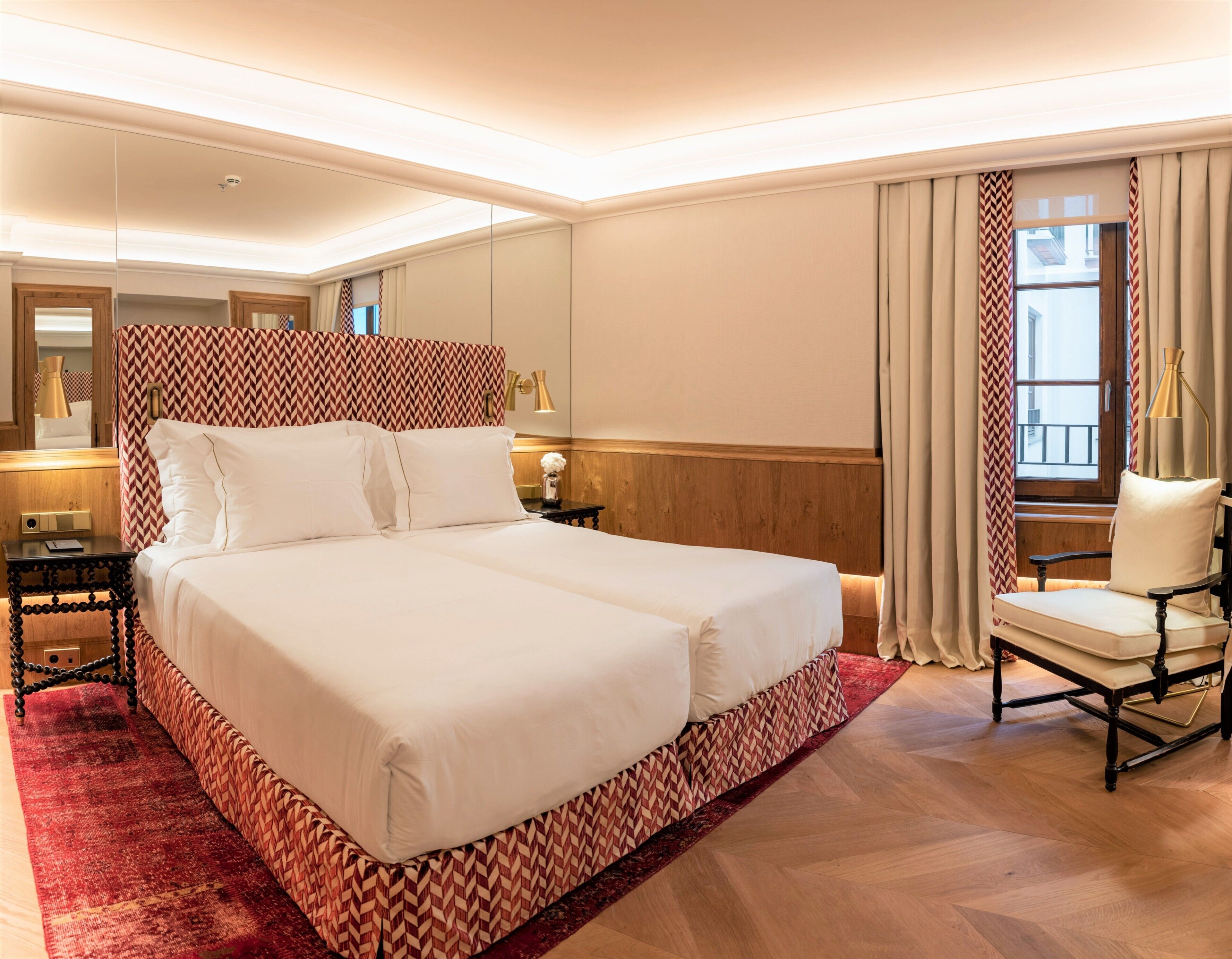 A hotel room with a large bed, a chair, a nightstand, a lamp, and a window with curtains.
