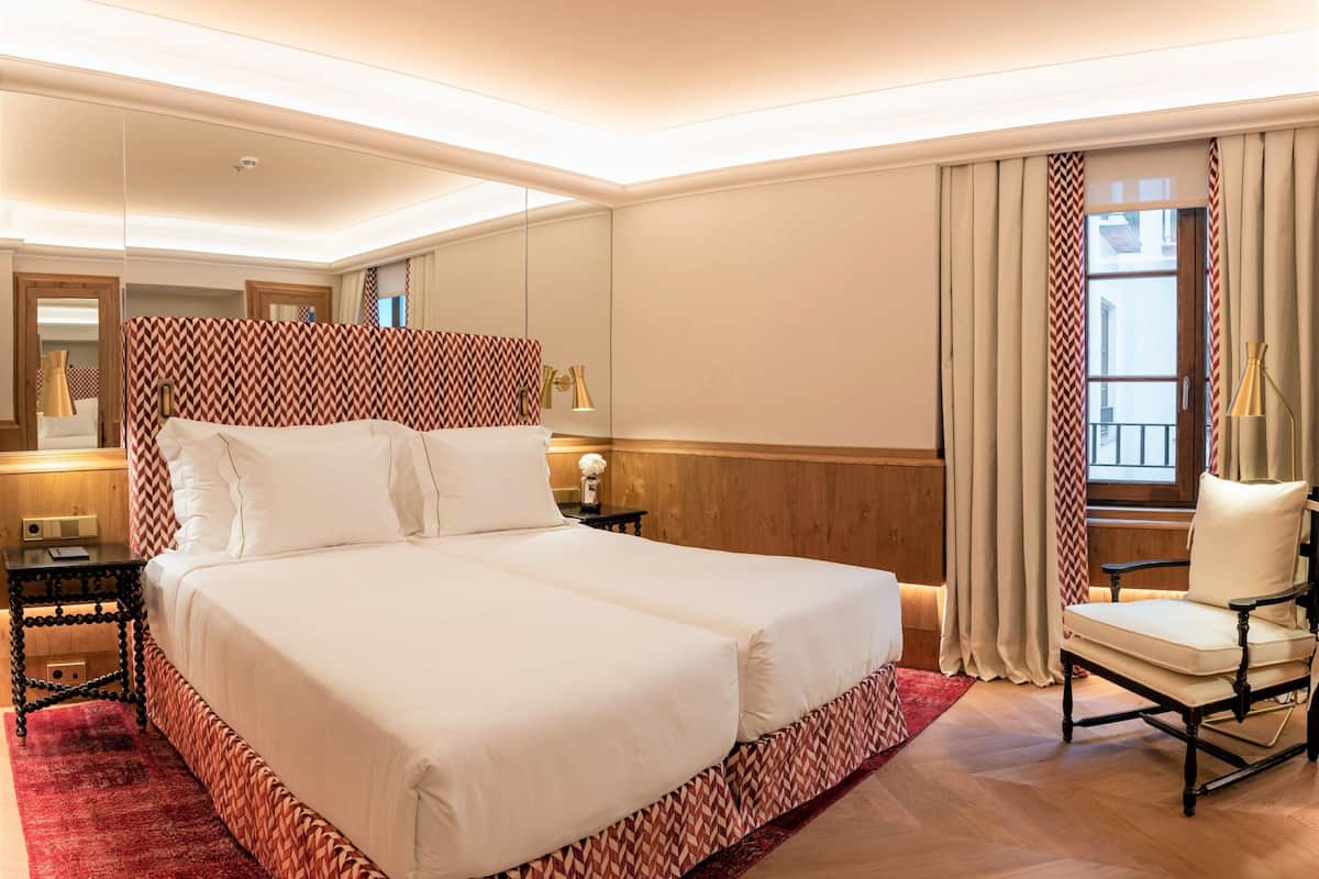 A hotel room with a large bed, a chair, a nightstand, a lamp, and a window with curtains.