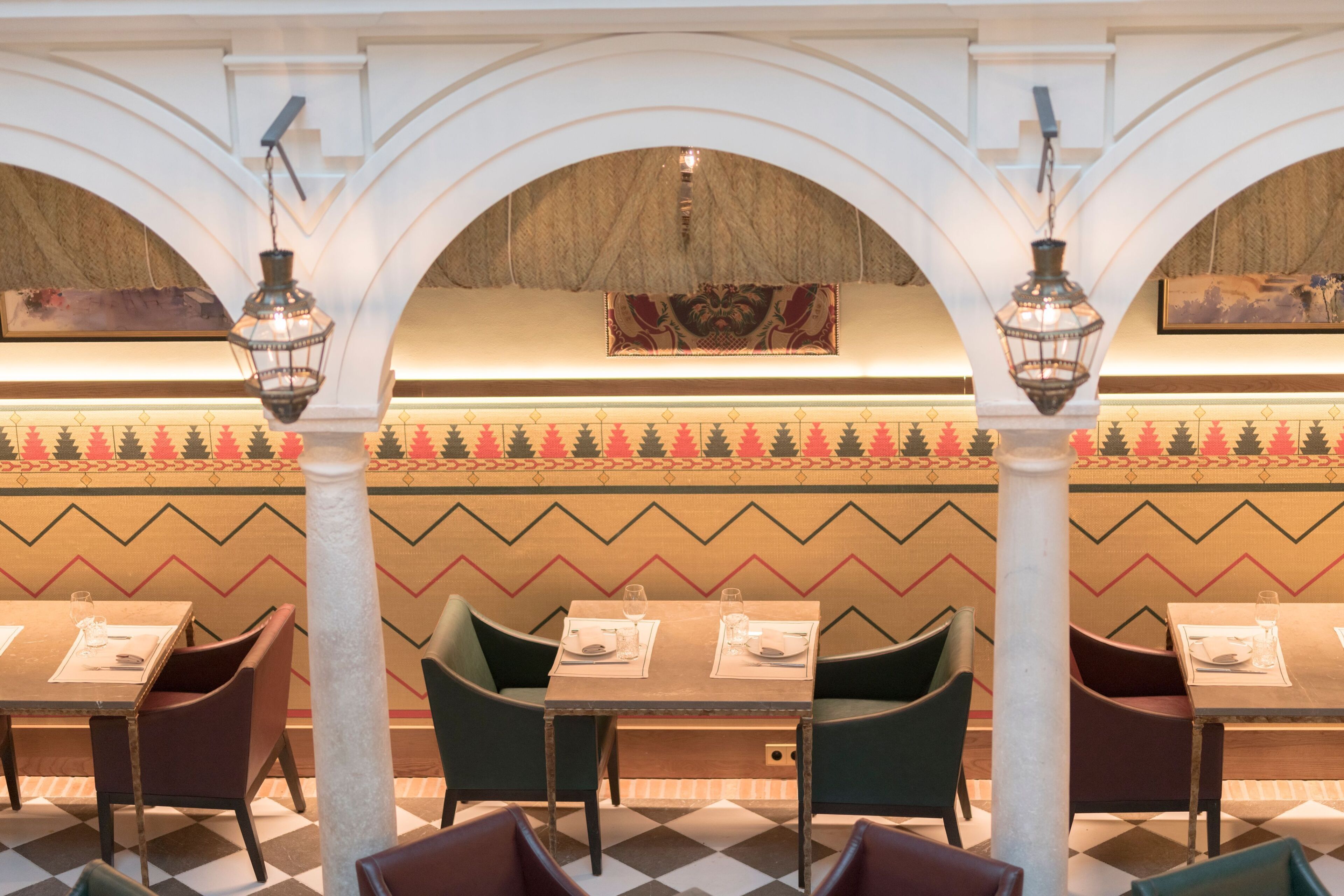 Un restaurante con mesas y sillas, diseños decorativos en las paredes y faroles colgantes.