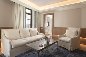 A hotel room with a sofa, armchair, and a small table with a bottle of champagne and glasses.