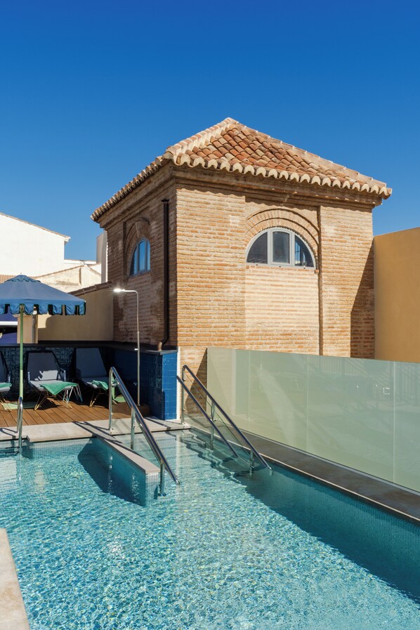 Piscina com barreira de vidro, um pequeno edifício de tijolo com telhado telhado e céu azul claro.