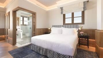 Habitación de hotel con una cama grande, una mesita de noche con lámpara, una ventana con cortinas estampadas y una puerta que da al baño.