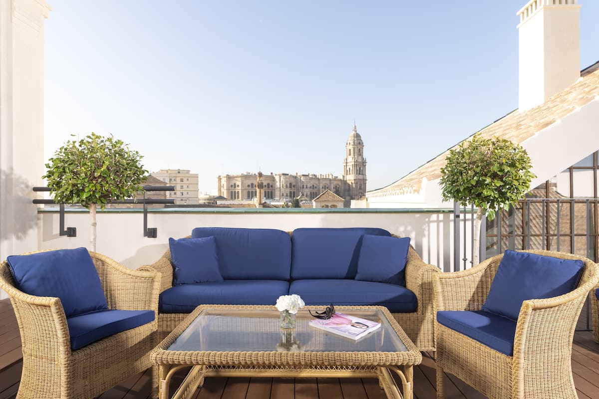 A balcony with wicker furniture, a glass table, and a view of a cityscape with a prominent building.