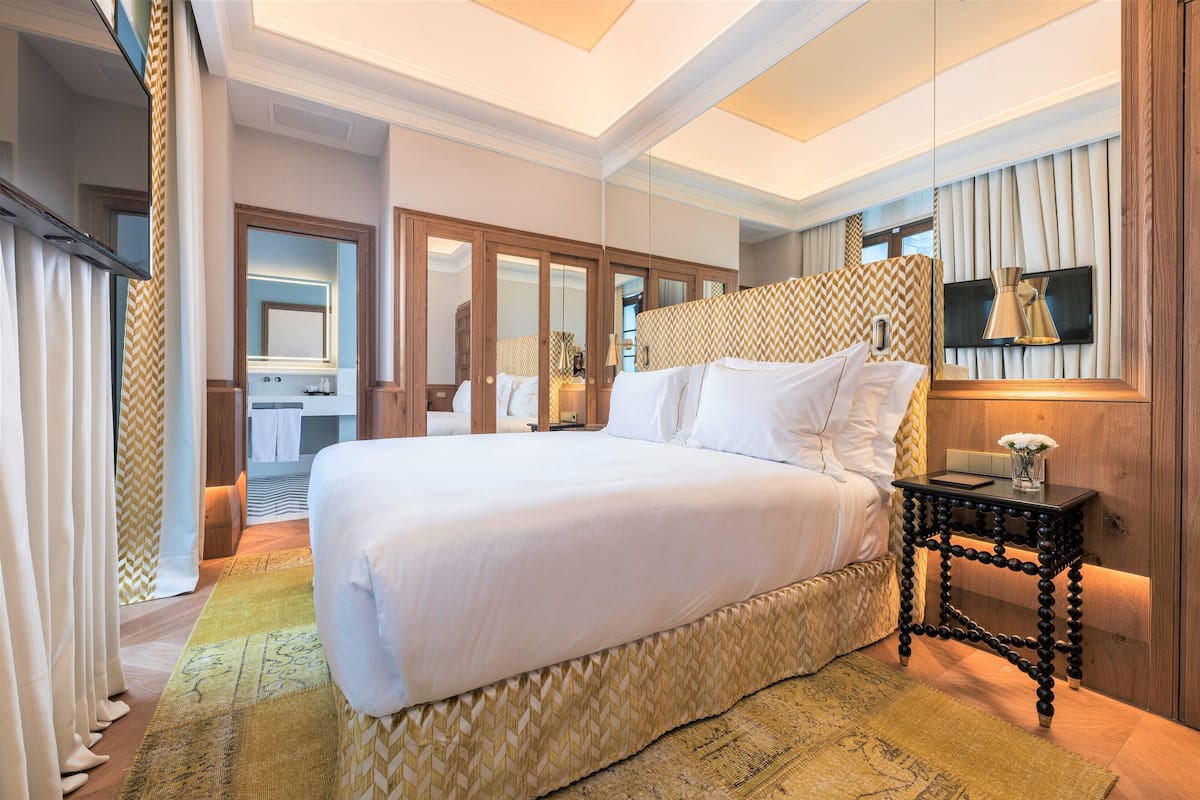 A hotel room with a large bed, a bedside table with a lamp, a mirror, and a television.