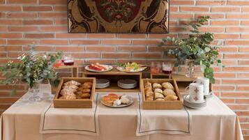Una mesa de buffet con diversos alimentos y bebidas, frente a una pared de ladrillo con un tapiz decorativo.