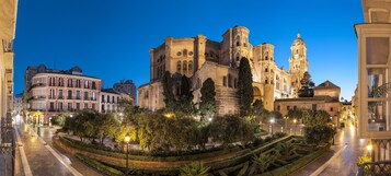 A historic cathedral with a prominent bell tower, surrounded by well-maintained gardens and adjacent urban buildings.