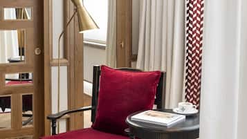 A red velvet chair with a black frame, a small round table with a book and a cup, and a floor lamp.