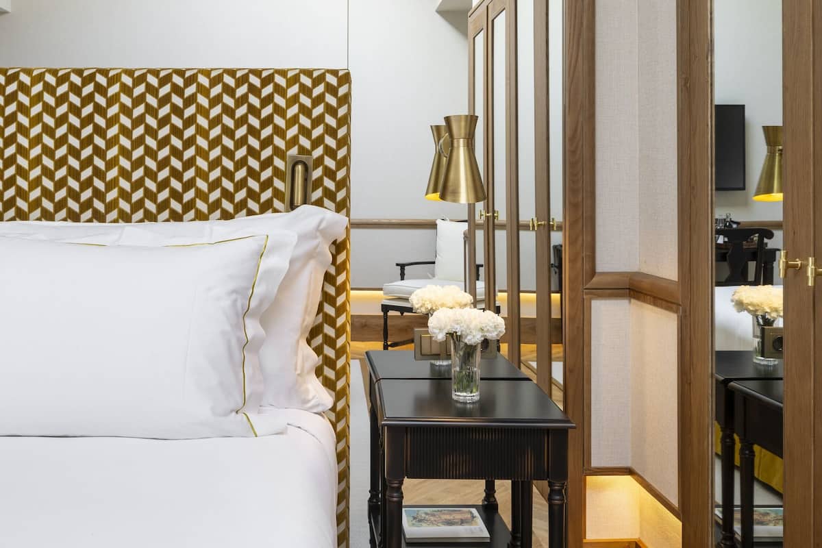 A hotel room with a bed, a bedside table with a lamp, a mirror, and a patterned headboard.