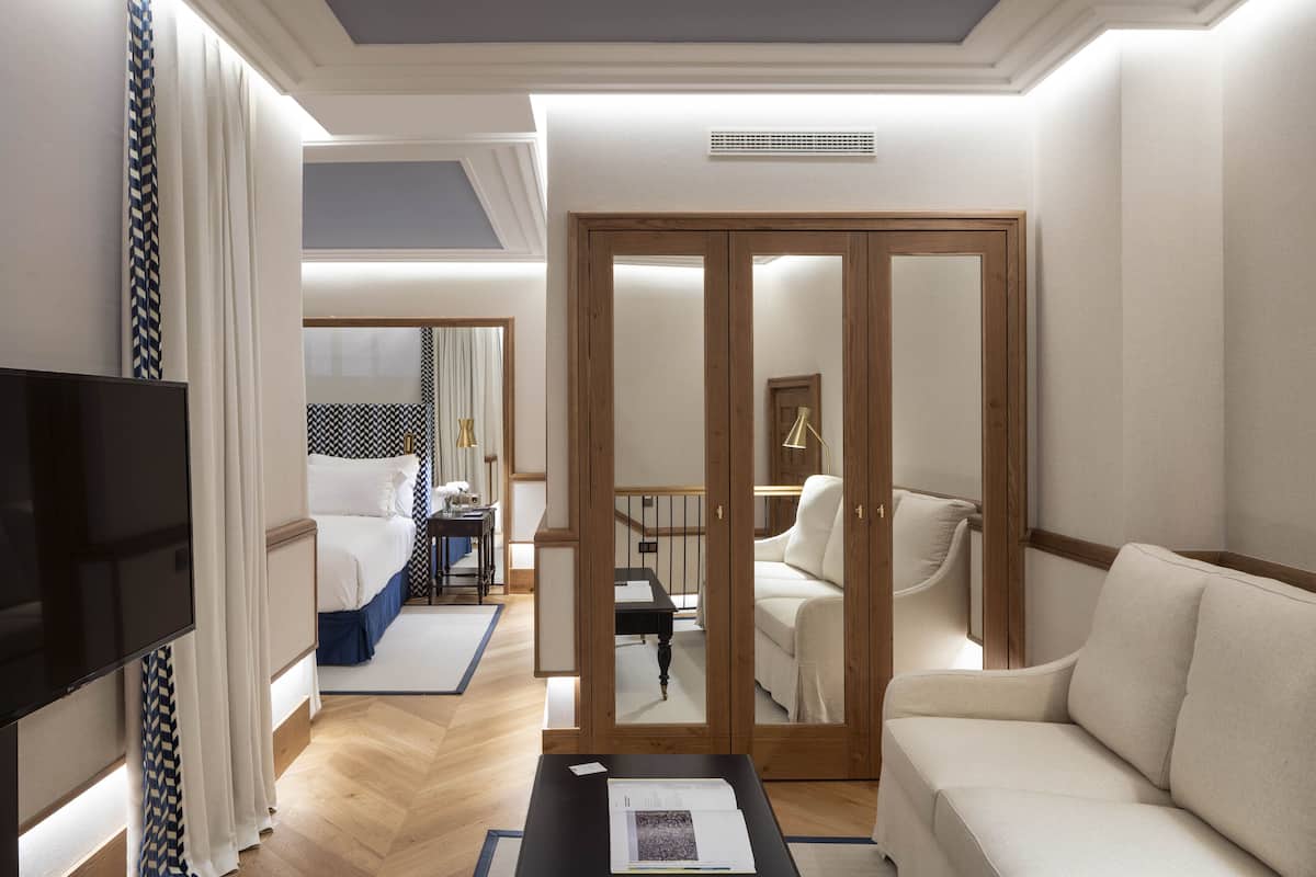 A hotel room with a bed, a TV, a sofa, and a wooden wardrobe.