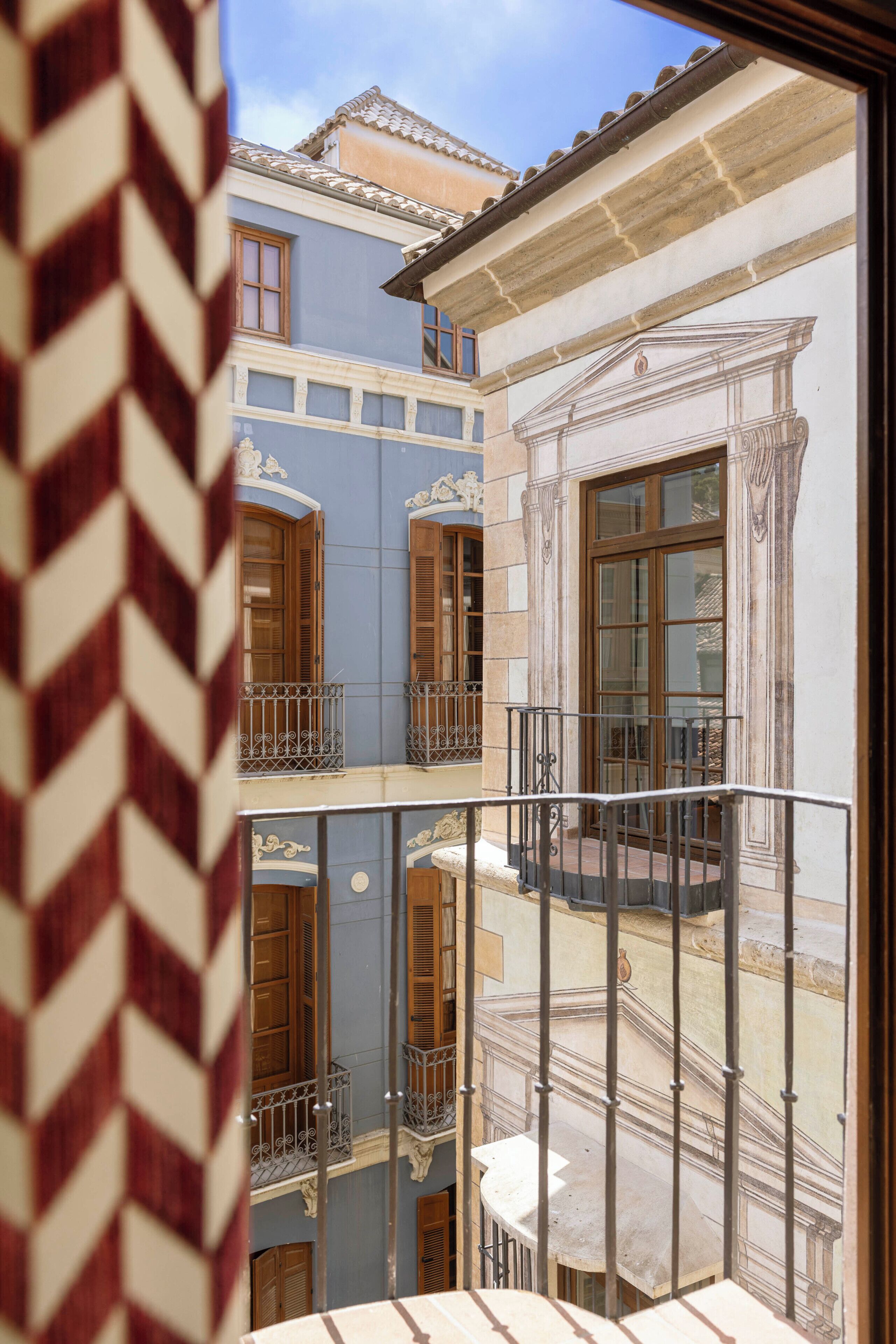 A multi-story building with balconies, a window with a decorative frame, and a view of the sky.