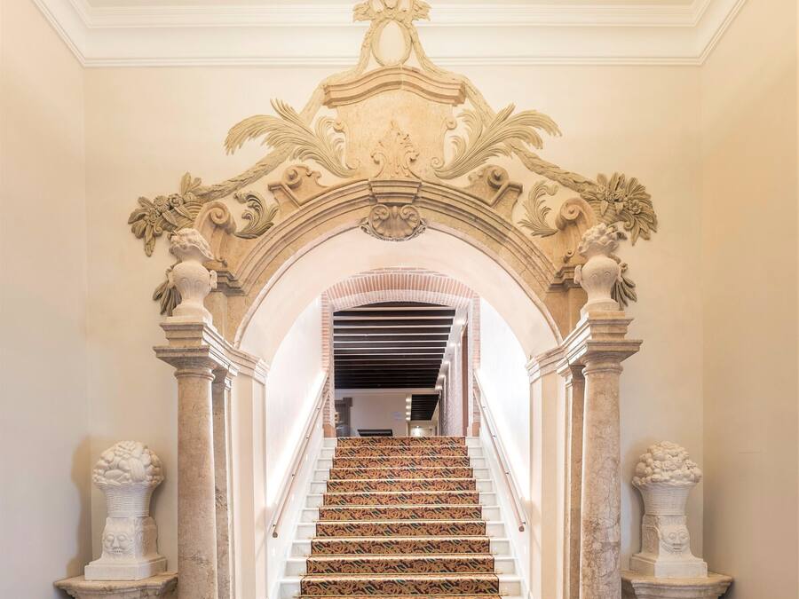 Una imponente escalera con intrincados adornos y un elegante suelo estampado, que conduce a una habitación con techo alto y molduras decorativas.