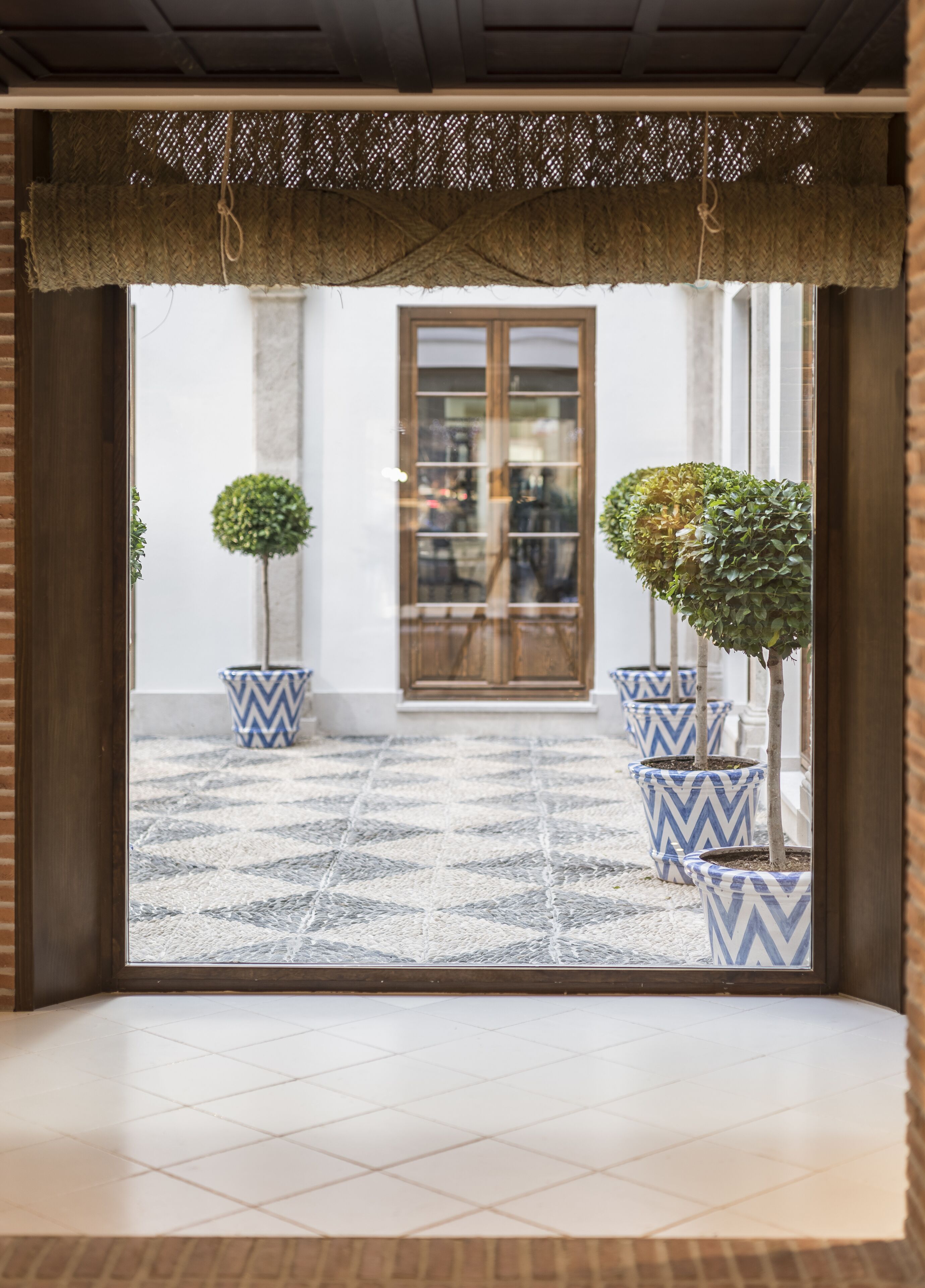 A doorway with a patterned floor leading to a room with a large wooden door and a view of the street.