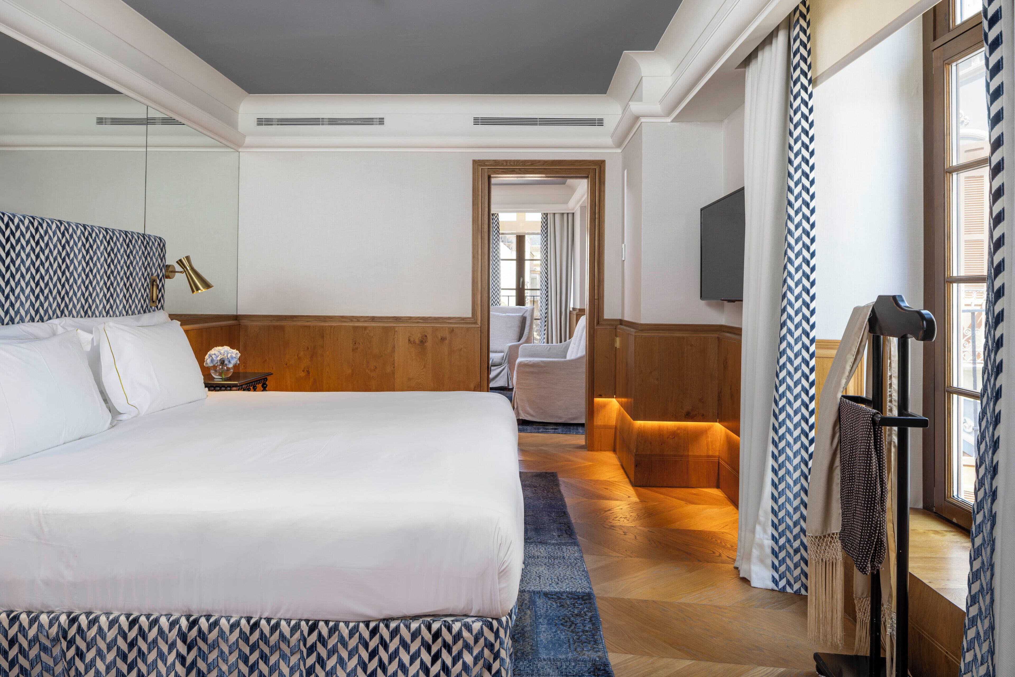 Quarto de hotel com uma cama grande, área de estar, televisão e vista para o exterior.