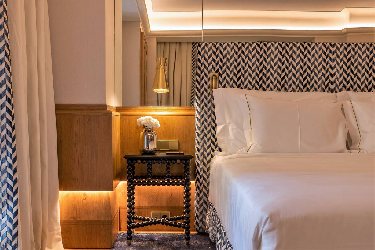 A hotel room with a bed, a nightstand with a lamp, and a patterned wall.