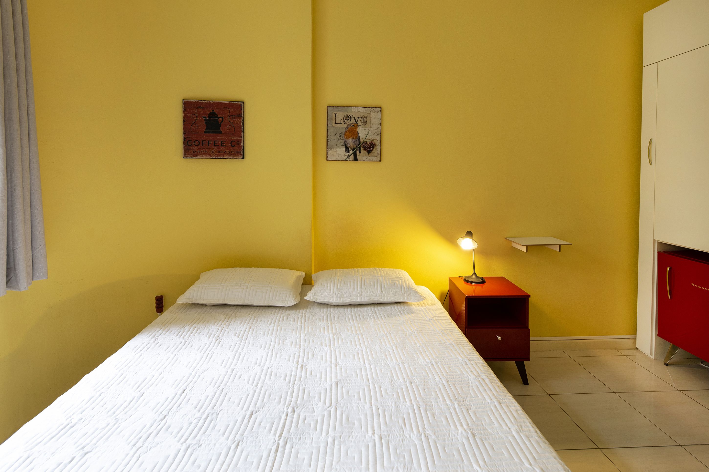 A single bed with white bedding, a nightstand with a lamp, and two wall-mounted pictures.