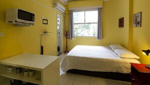 A yellow room with a bed, a desk, a microwave, and a window. - Rio Rentals 021 - C005 Studio em Copa (Rio de Janeiro)