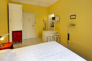 A hotel room with a bed, a desk, a red minibar, a microwave, and a mirror. - Rio Rentals 021 - C005 Studio em Copa (Rio de Janeiro)