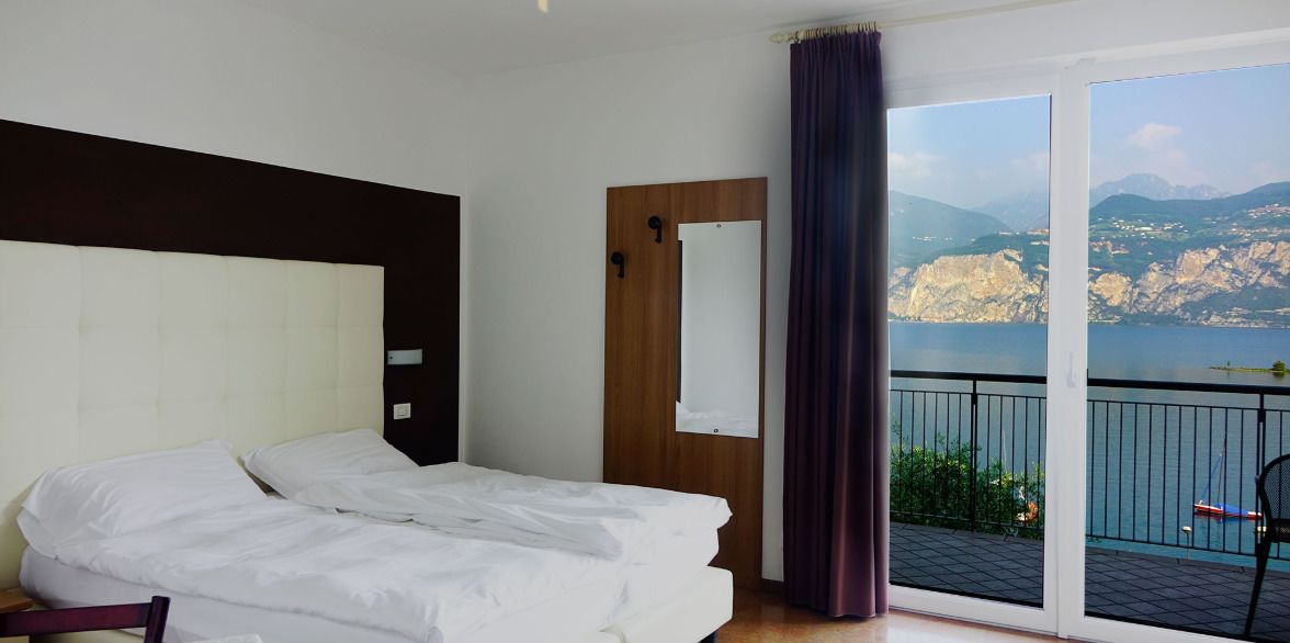 Une chambre d’hôtel avec un grand lit, une tête de lit en bois et une porte-fenêtre coulissante donnant sur un balcon avec vue sur la montagne.