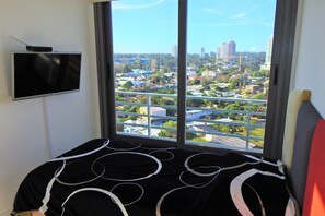 A bedroom with a large window, a flat-screen TV mounted on the wall, and a bed with a black and white patterned bedspread. - Apartment Alexander Boulevard (Punta del Este)