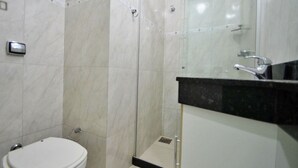 A bathroom with a toilet, a shower enclosure, and a sink with a mirror. - Rio Rentals 021 - C073 Studio com Vista Mar (Rio de Janeiro)