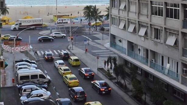 A busy street with cars and a building with balconies overlooking a beach. - Rio Rentals 021 - C073 Studio com Vista Mar (Rio de Janeiro)
