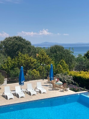 A poolside area with lounge chairs and umbrellas, surrounded by lush greenery and a view of the sea. - Siesta Otel Bozcaada (Bozcaada)