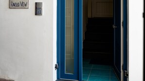 Puerta de marco azul con un panel de vidrio, una placa pequeña con un dibujo y texto, y un felpudo azul en la entrada.