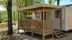 Une petite cabane en bois, dotée d’un porche et d’une fenêtre, entourée d’arbres.