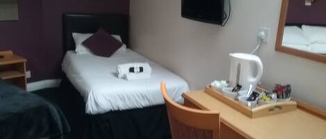 A hotel room with a bed, a desk, a chair, a TV, and a coffee maker.