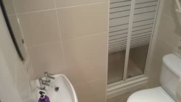 Un baño con lavamanos blanco, inodoro y ducha con puerta de cristal.
