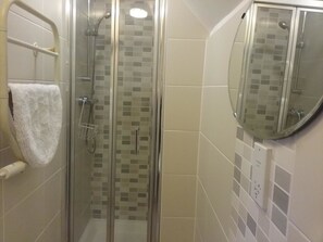 A glass-enclosed shower with a white towel hanging on a rack, a showerhead, and a tiled wall with a small mirror. - The Prince Consort (Southampton)