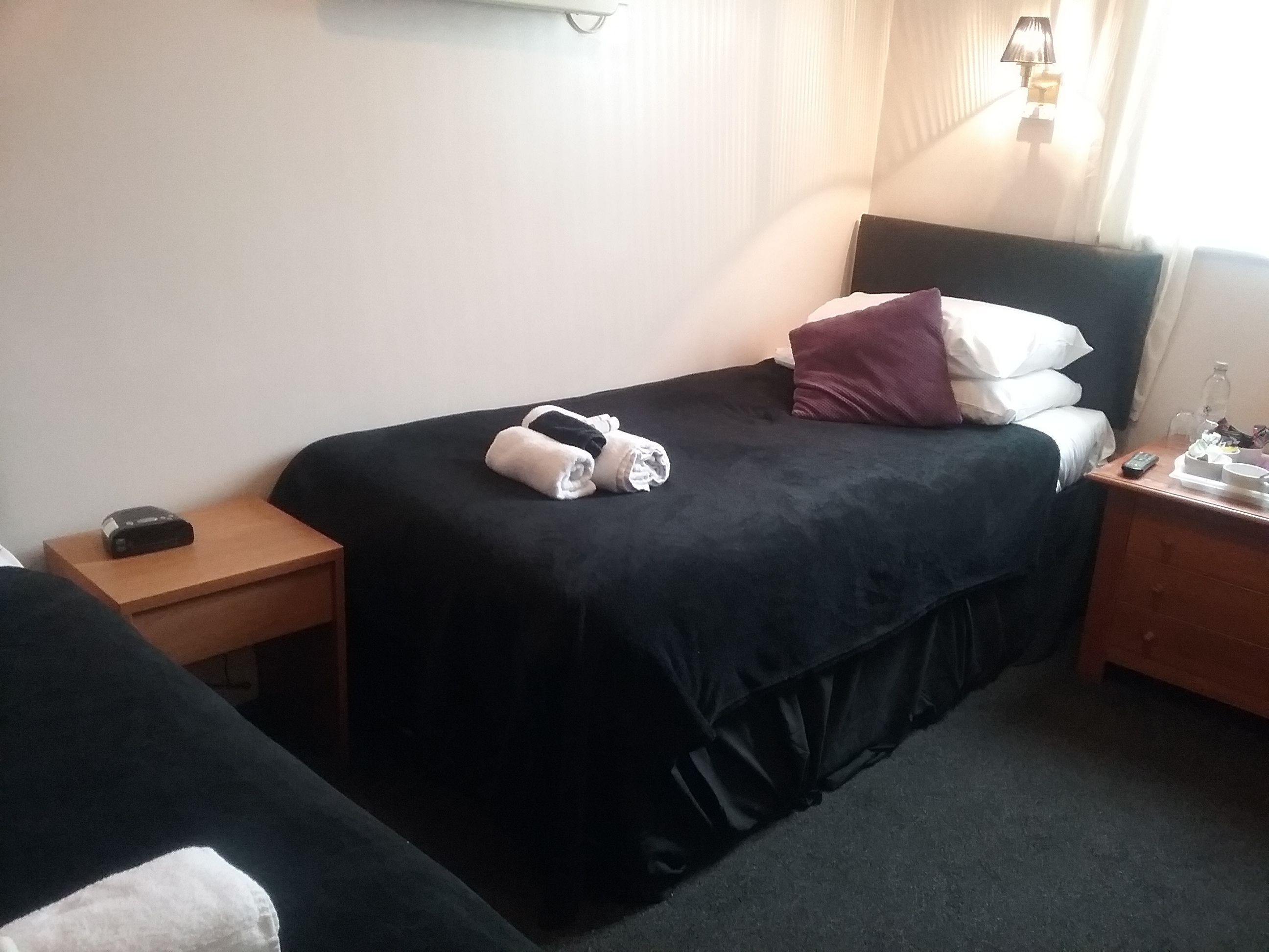 A hotel room with a bed, a bedside table, a nightstand, and a lamp.