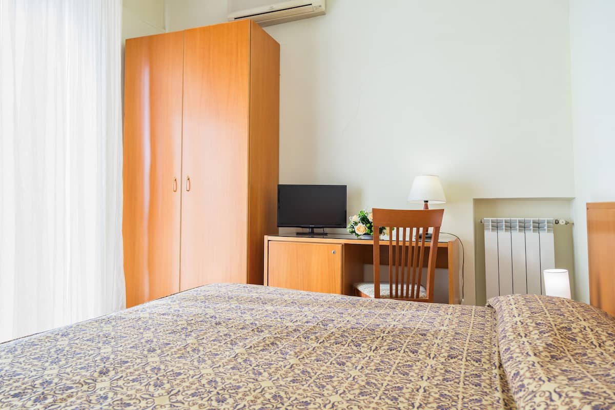 Une chambre d’hôtel avec un lit, un bureau avec une télévision, une chaise et un radiateur.