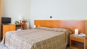 Een hotelkamer met een houten hoofdeinde, een bed met een geborduurde spreideken, een bureau met een televisie, een lamp en een telefoon.