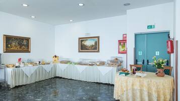 Une salle de conférence avec une longue table recouverte d’une nappe blanche, divers plats et deux tableaux encadrés accrochés aux murs.