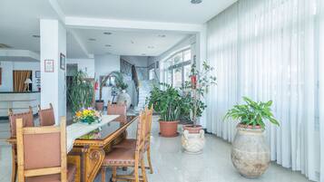 Uma ampla sala de jantar com uma mesa e cadeiras de madeira, cercada por plantas em vasos e um vaso grande.