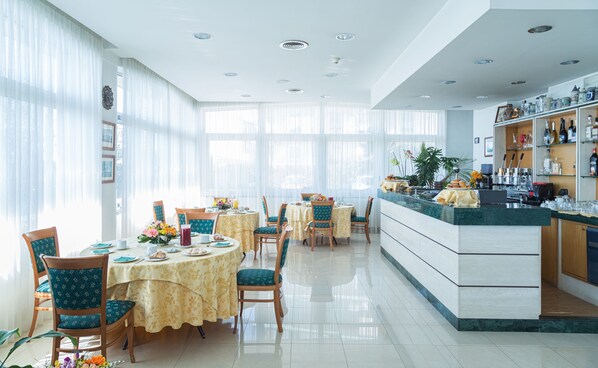 Un comedor luminoso con mesas redondas, sillas y una encimera de cocina con diversos objetos.